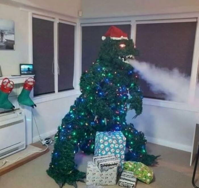 Christmas tree decorated as a Godzilla figure with lights and a Santa hat, blowing mist in a living room with presents.