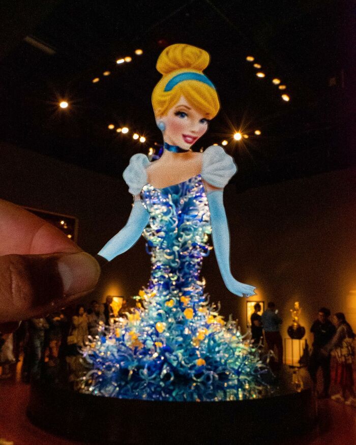 Hand holding a paper cutout of Cinderella in a sparkling blue dress, showcasing brilliant paper cutouts by Rudy Willingham.