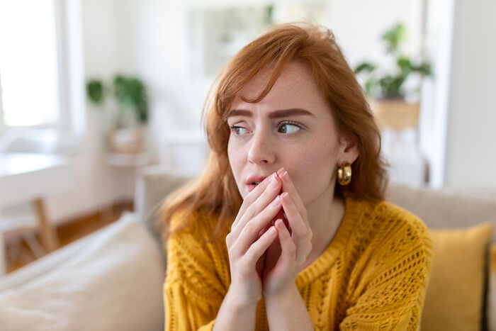 Young woman in a yellow sweater looking worried indoors, showing signs a child was never loved properly through facial expression.
