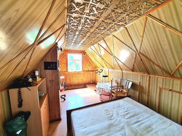 Attic bedroom with wooden paneling and patterned ceiling in a wild real estate listing showing unique interior design.