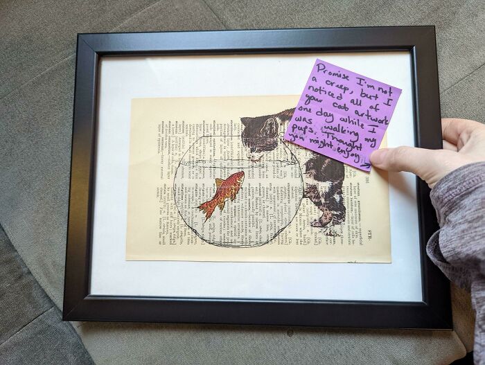 Framed artwork of a cat looking at a goldfish with a handwritten note, showing faith in humanity restored moments.