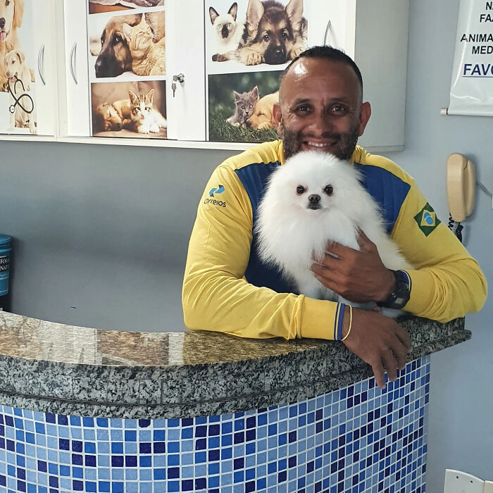 Mailman smiling and holding a fluffy white dog, showcasing friendship with dogs on his mail route.