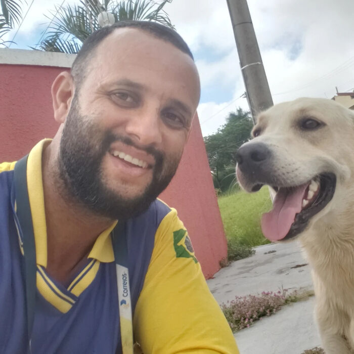 Mailman smiling and posing with a happy dog on his route, showing friendship between mailman and every dog.