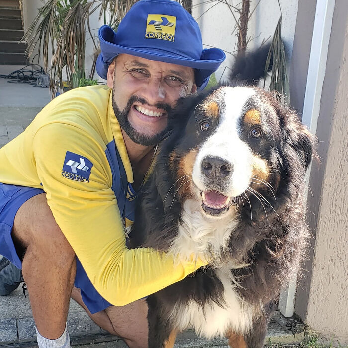 Mailman smiling and hugging a large dog, showing friendship and bond during his delivery route.