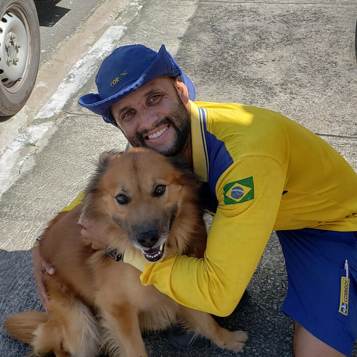 Mailman in yellow uniform happily hugging a friendly dog on his delivery route outside on the pavement.