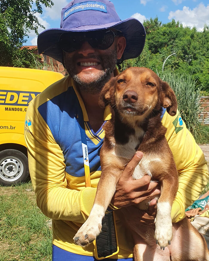 Mailman smiling and holding a brown dog, showcasing the bond between mailman and dogs on his route.