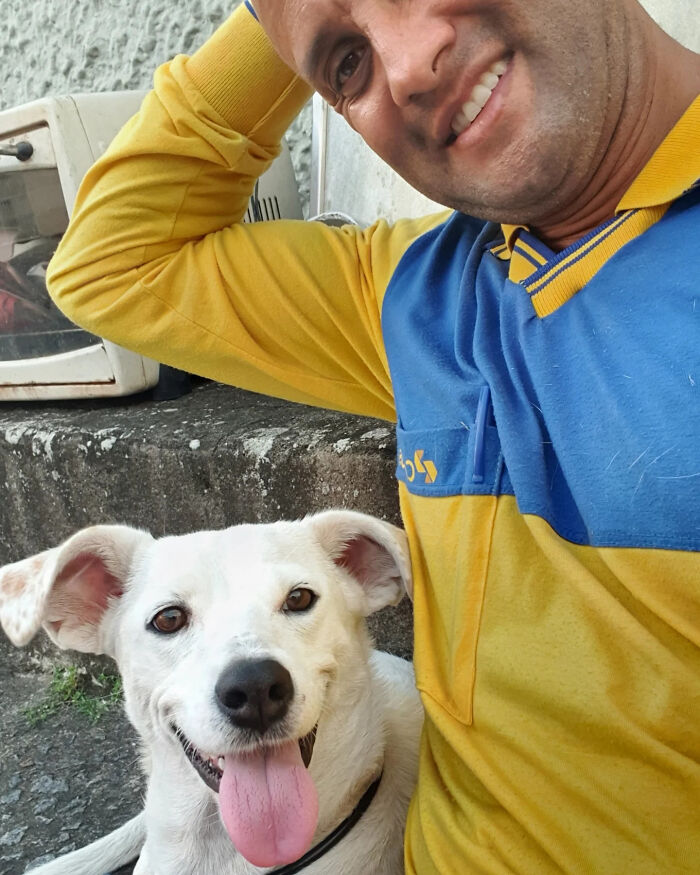 Mailman smiling and posing with a happy white dog, showcasing his friendly bond with dogs on his route.