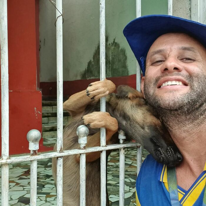 Mailman smiling with a dog leaning through metal bars, showing friendship on his delivery route.