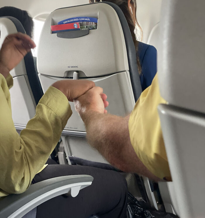 Two strangers holding hands on an airplane, showing faith in humanity and kindness during travel.