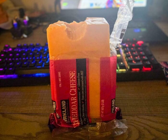 Block of cheddar cheese with a bite taken out, sitting on a desk as part of iconic girl dinner combos.