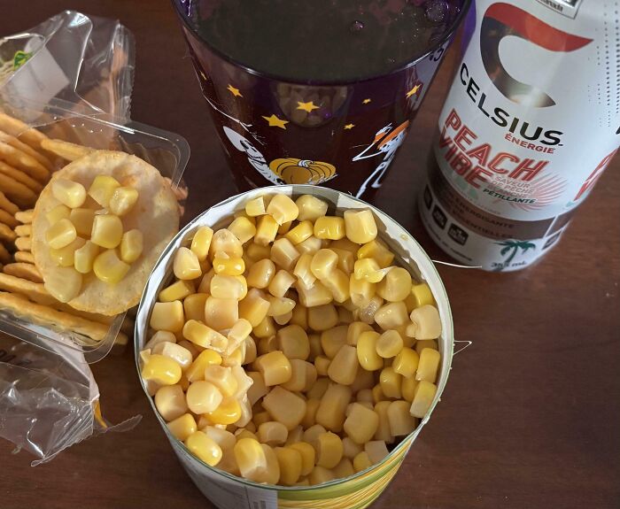Open can of corn, crackers with corn, a drink in a Halloween cup, and a can of peach-flavored energy drink girl dinner combo