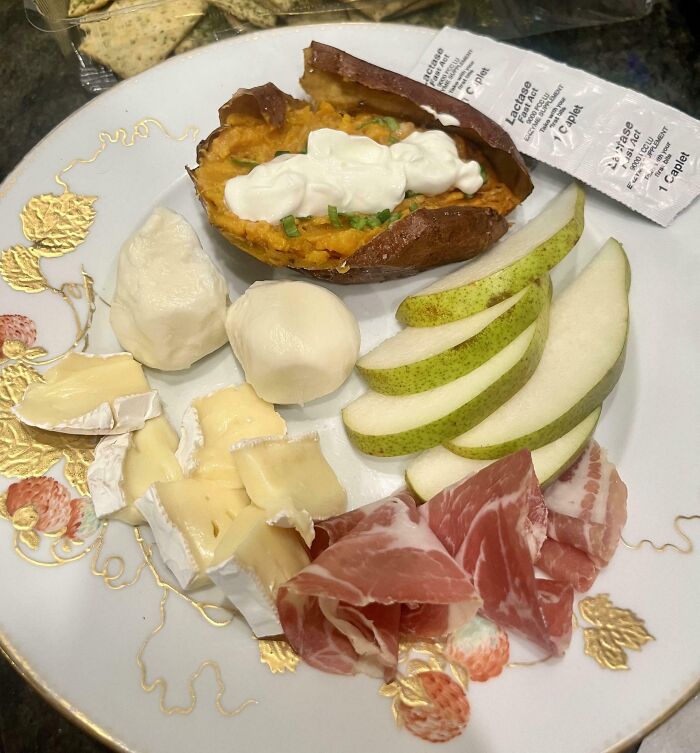 Plate with sweet potato topped with sour cream, sliced pear, cheese, prosciutto, and crackers, girl dinner combos.
