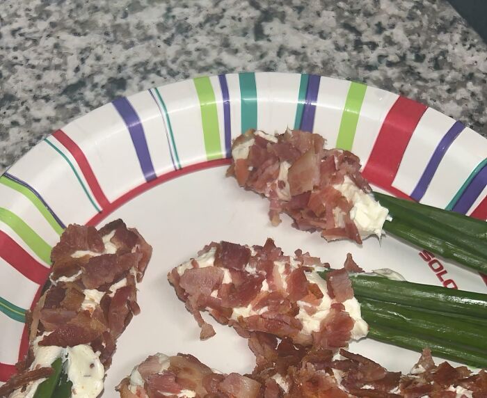 Green onions coated with cream cheese and bacon pieces on a colorful paper plate, a popular girl dinner combo.