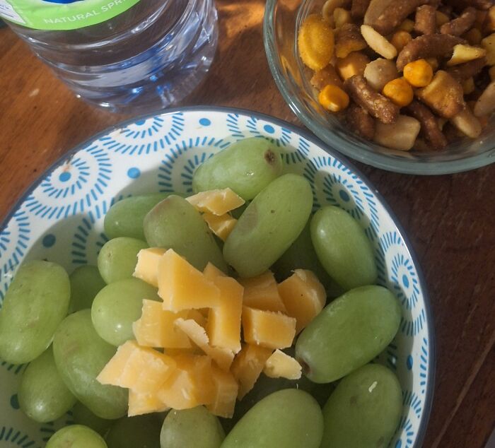 Bowl of green grapes with cheese cubes and a snack mix beside a bottle of water, representing girl dinner combos.