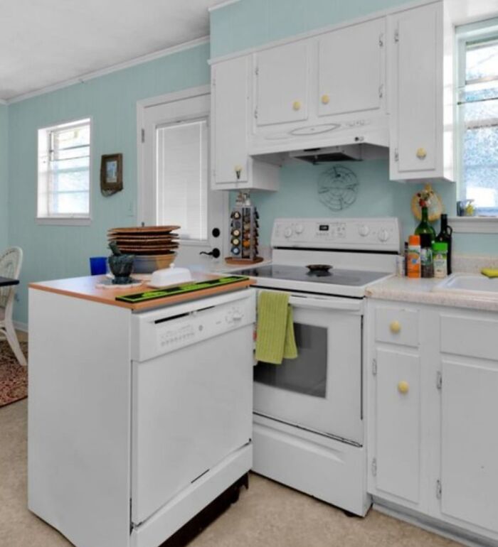 Bright kitchen in Zillow home with white appliances, cabinetry, and pastel blue walls showcasing unique real estate charm.