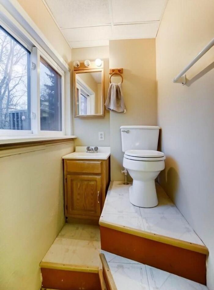 Small unique bathroom layout in Zillow home listing featuring a raised toilet platform and compact vanity with window view.