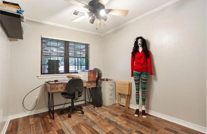 Unusual Zillow home interior with a mannequin wearing festive clothes in a simple office space.