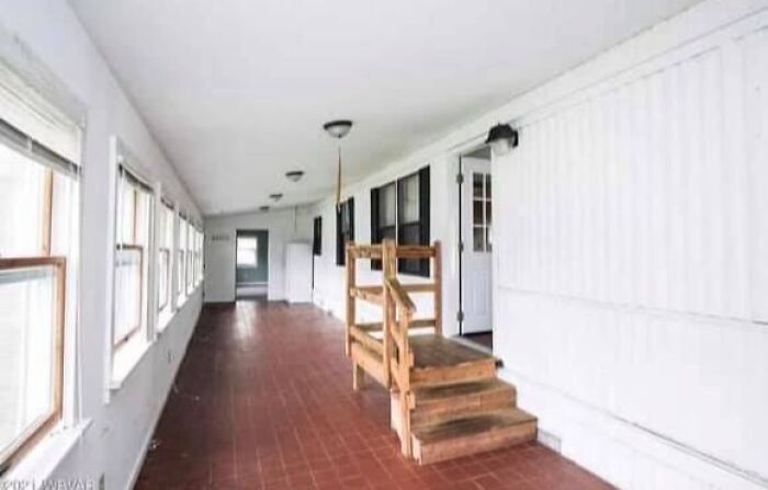 Long enclosed porch with multiple windows and wooden steps leading to a door in a Zillow home interior.
