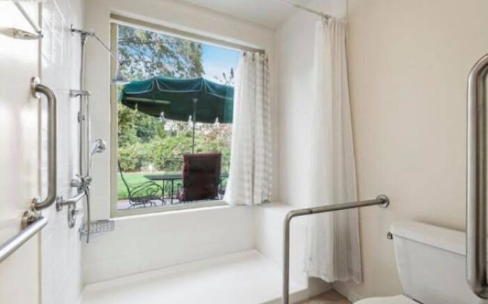 Bright bathroom in a Zillow home with large window, garden view, and accessibility grab bars for safety and comfort.