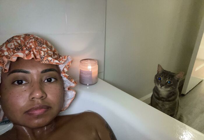 Person in bathtub wearing a shower cap with a cat nearby illustrating losing personal space after getting a pet.