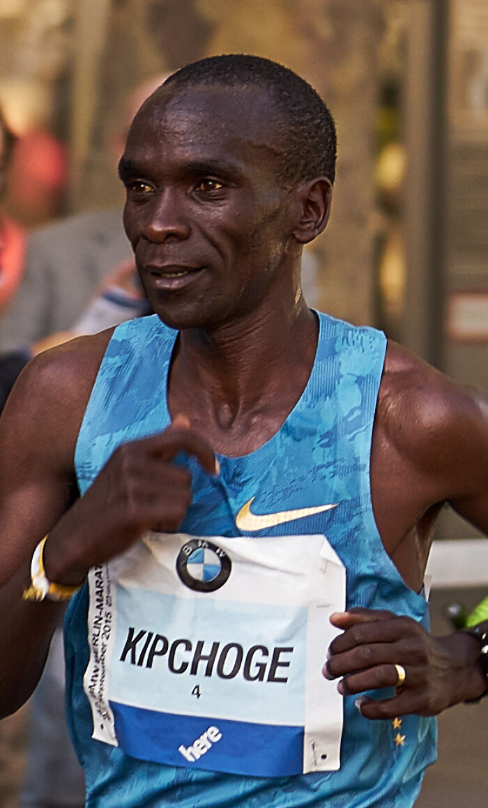 Eliud Kipchoge running in a blue Nike tank top during a marathon, showcasing his athletic endurance and focus.