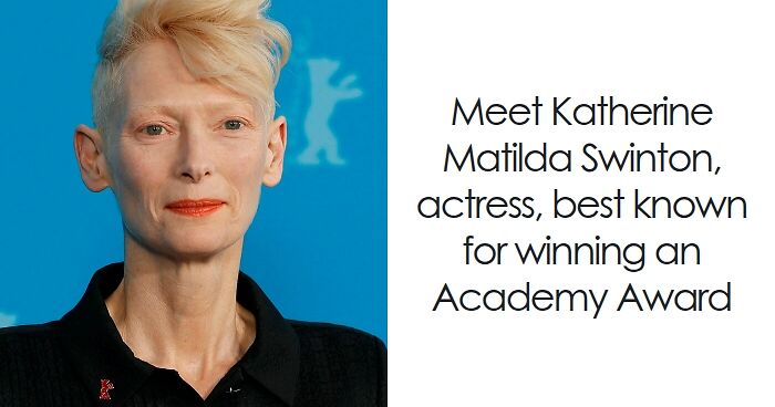 Tilda Swinton with short blonde hair, wearing a black top, against a blue background at a film event.