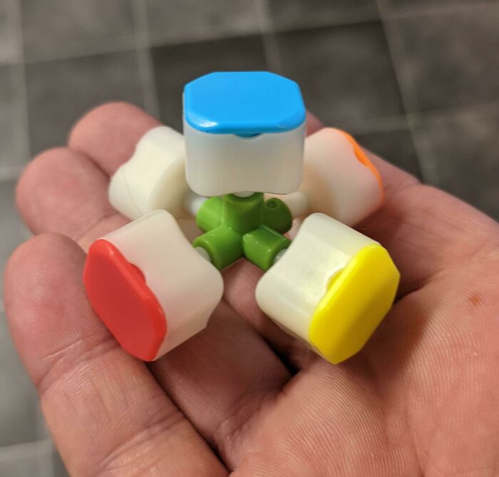 Hand holding a small mechanical object showing the insides of a colorful multi-headed connector, revealing inner parts.