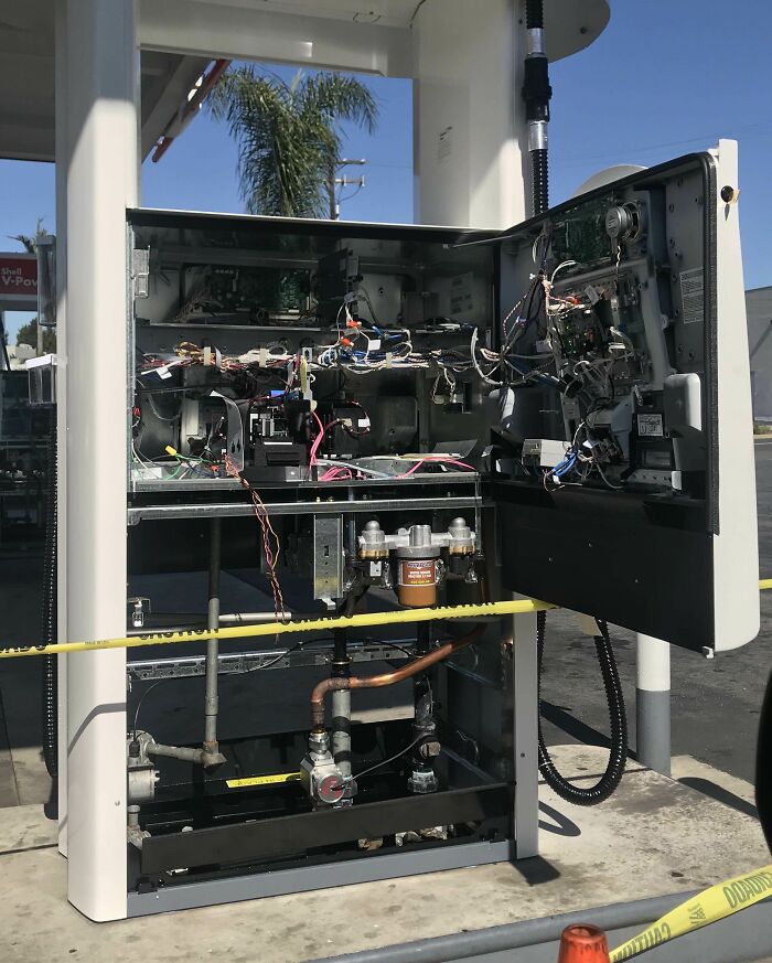 Inside view of a complex gas pump system showing internal wiring, pipes, and mechanical components at a gas station.