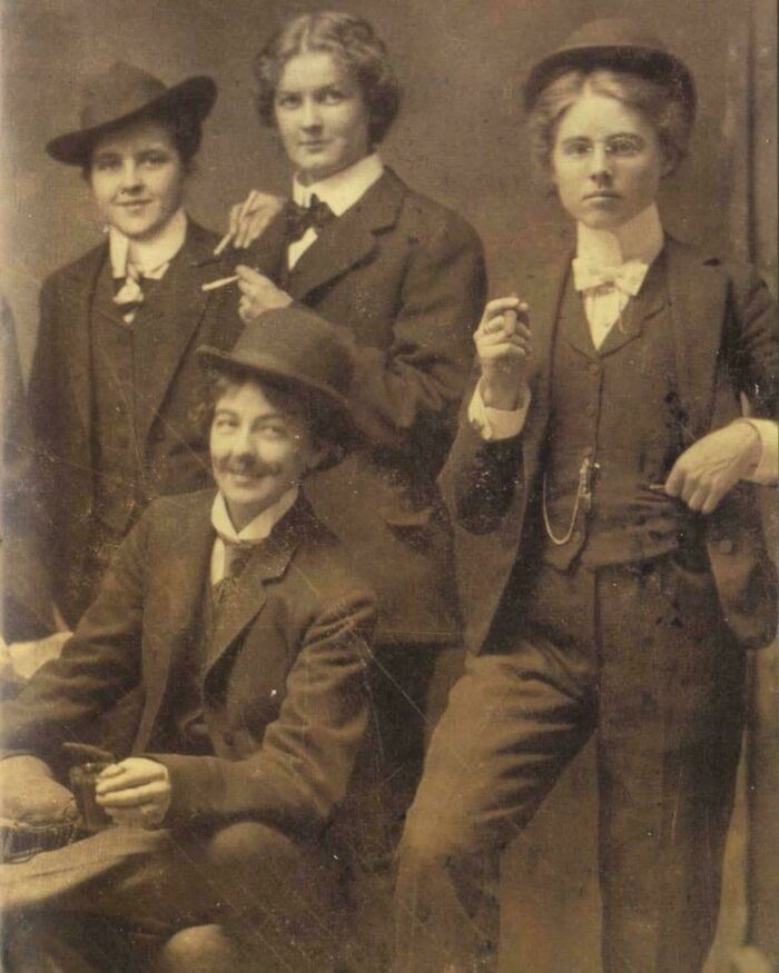 Group of four young people in Victorian-Edwardian pictures wearing period suits and hats, some holding cigarettes.