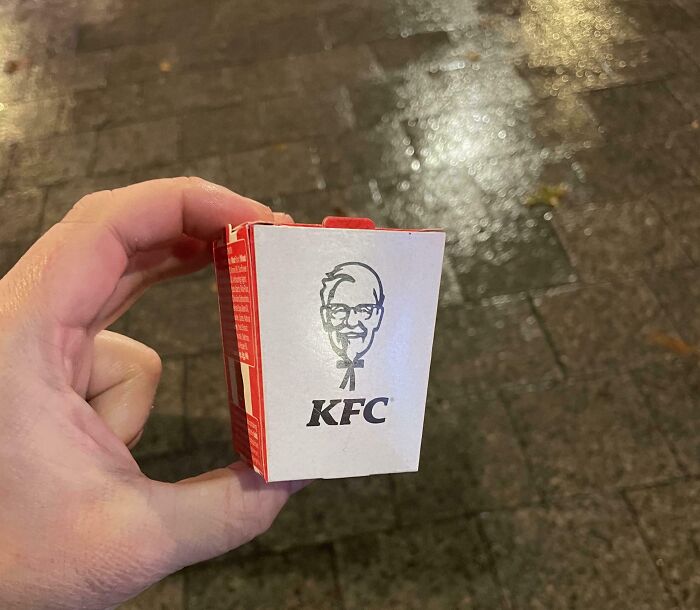 Hand holding a miniature KFC chicken box, showcasing misleading packaging by companies selling smaller products.