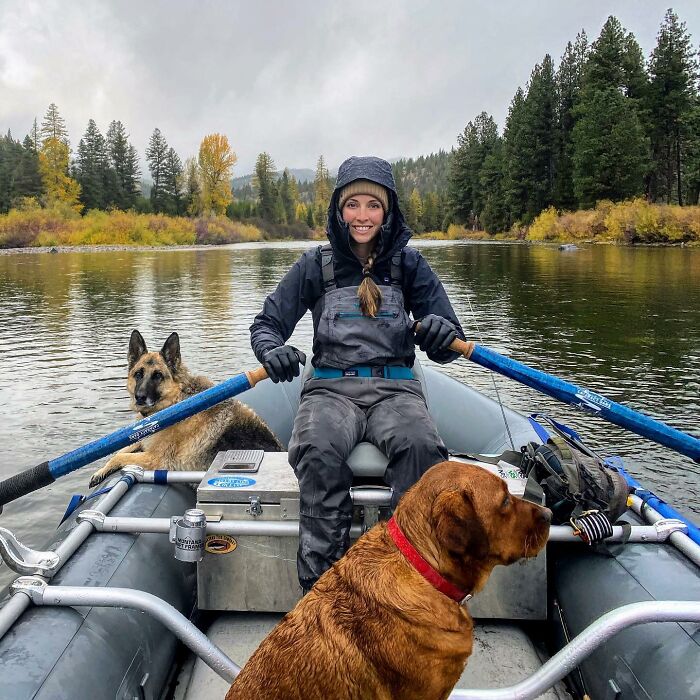 Woman rowing a boat with two dogs, one being Leo, a dog rejected from service dog training, on a calm river surrounded by trees. Woman rowing a boat with two dogs, one being Leo, a dog rejected from service dog training, on a calm river surrounded by trees.