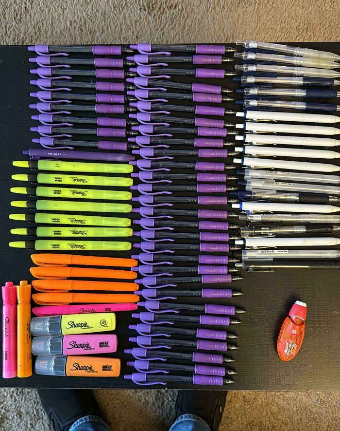 Neatly arranged pens, markers, and highlighters in rows showcasing satisfying order and organization on a black surface.