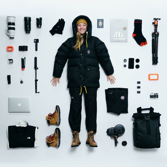 Woman in black winter clothes laying on floor with camera gear and hiking boots neatly arranged around her in knolled order