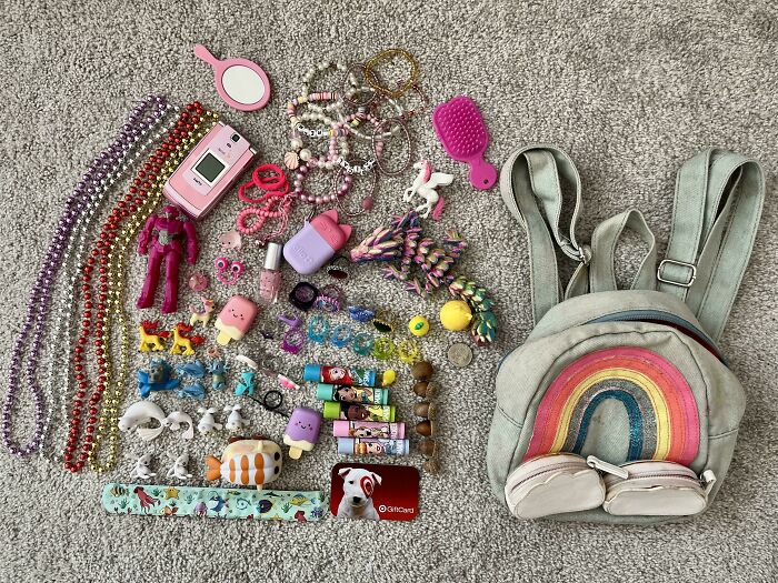 Colorful knolled assortment of toys, accessories, and a small backpack arranged neatly on carpet.