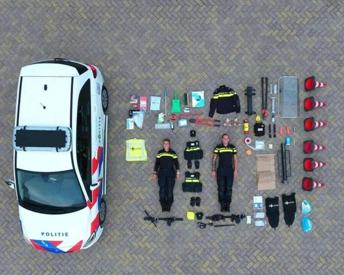 Police officers and gear neatly arranged in a knolled style next to a marked police car on a paved surface.