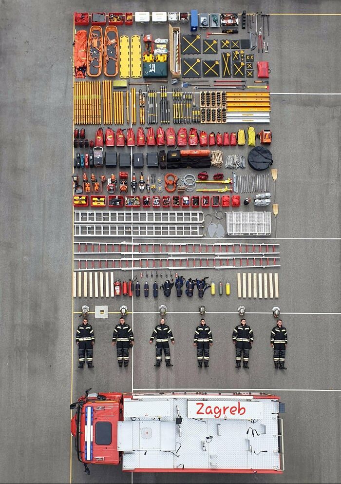 Firefighter gear, tools, and equipment neatly knolled and arranged alongside a fire truck and six firefighters in uniform.