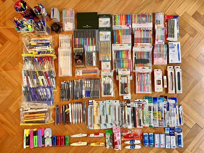 Assorted pens, markers, highlighters, and stationery neatly arranged on a wooden floor, showcasing knolled organization.
