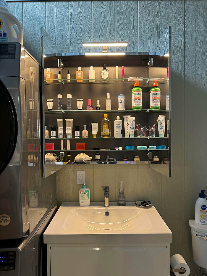 Neatly organized bathroom cabinet with skincare and hygiene products neatly arranged on shelves above a sink.
