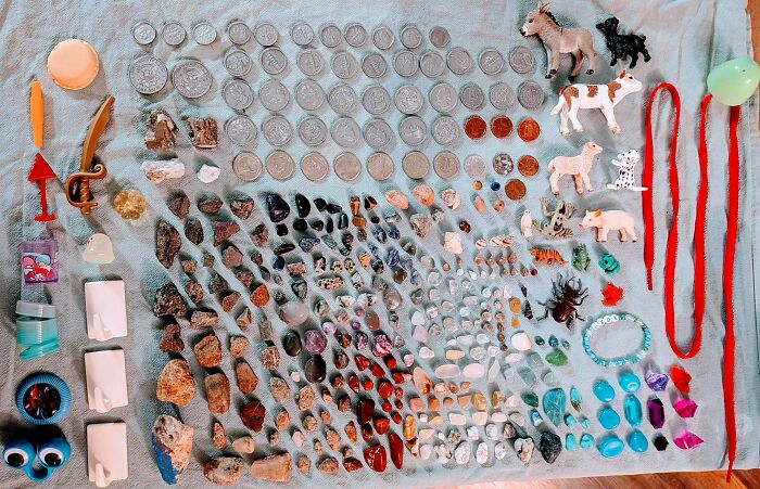 Neatly knolled collection of coins, rocks, toys, and colorful trinkets arranged by size and type on a fabric surface.