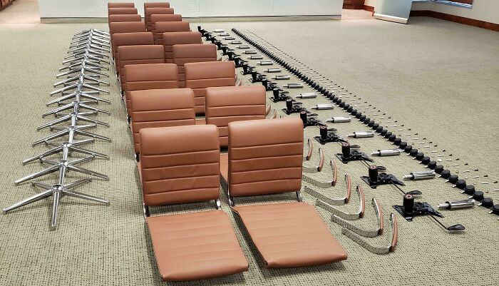 Rows of disassembled brown chair parts and metal bases neatly arranged on a beige carpet, showcasing order and organization.