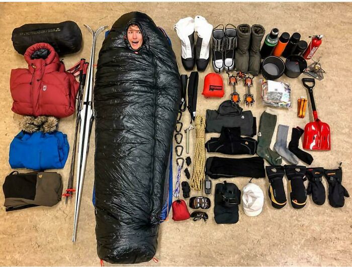 Person in a sleeping bag surrounded by neatly arranged outdoor gear, showcasing all things knolled and order.