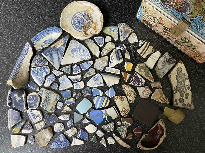 Broken ceramic pieces arranged neatly on a dark surface, showcasing satisfying order and knolled organization.