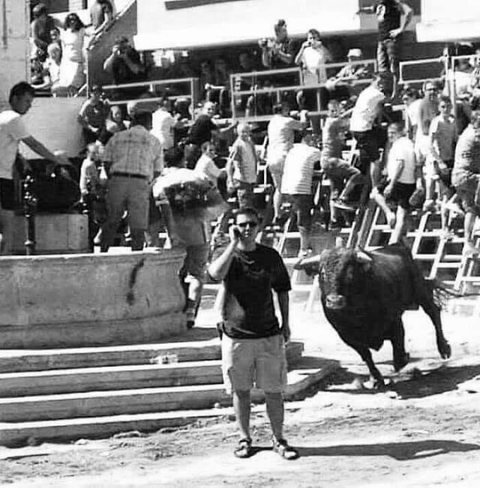 Man casually standing near a bull in a crowded arena, one of 84 frozen frames capturing moments before the aftermath.