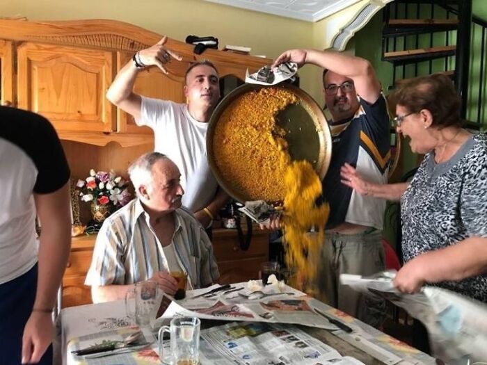 Group of people capturing a frozen frame as large food spills during a lively indoor gathering at a dining table.