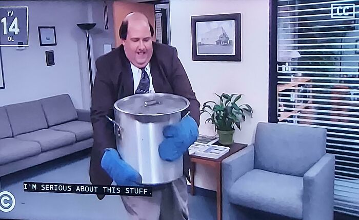 Man wearing oven mitts carrying a large pot indoors, a frozen frame capturing tension without showing aftermath