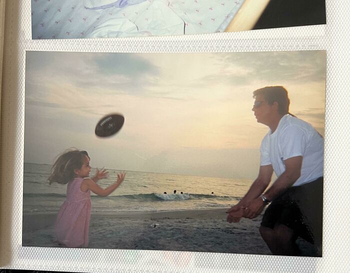 Young girl and man playing with a football on the beach, captured in a frozen frame at sunset.