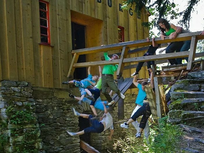 Group of people frozen mid-fall from a wooden balcony in an outdoor scene capturing dramatic frozen frames.