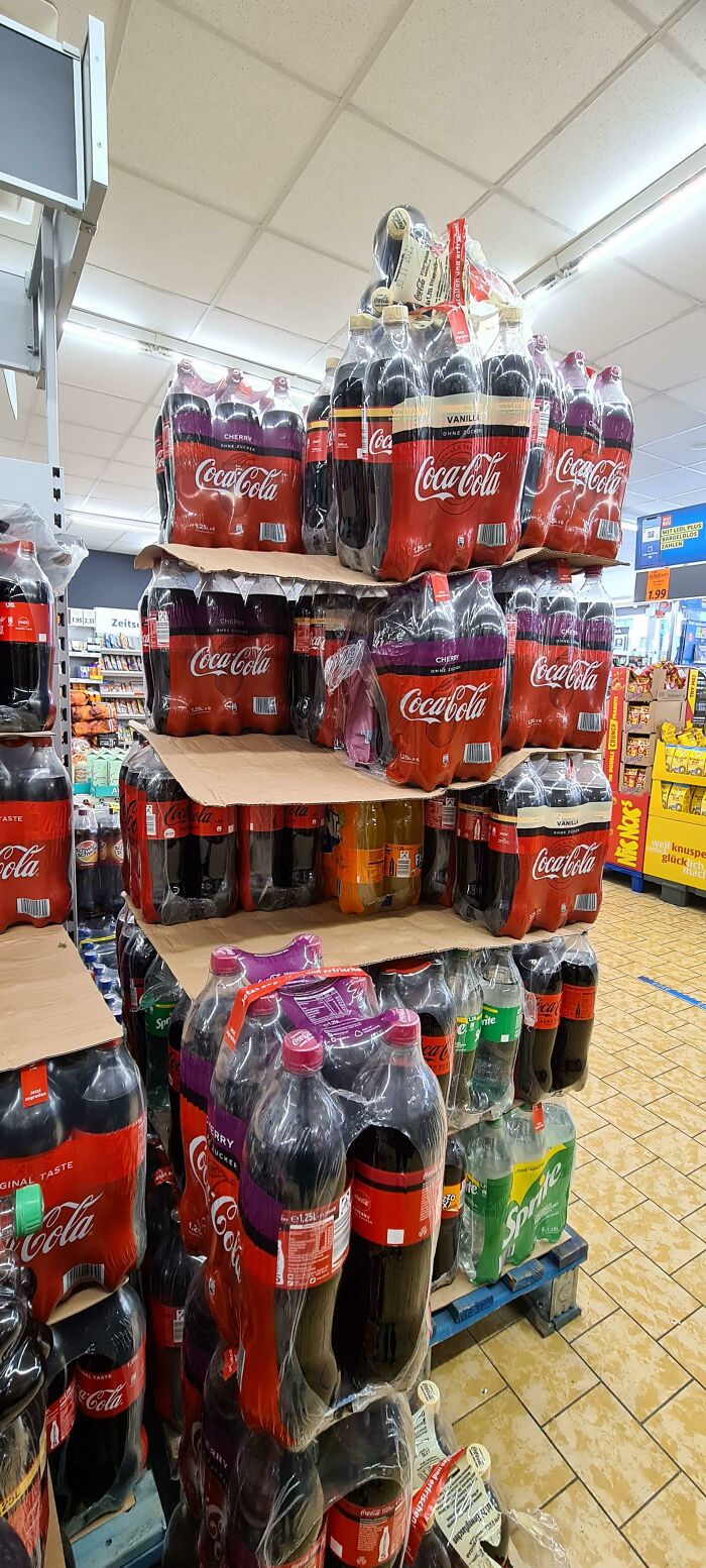 Stacks of Coca-Cola bottles and other soft drinks arranged on pallets in a grocery store frozen frames display