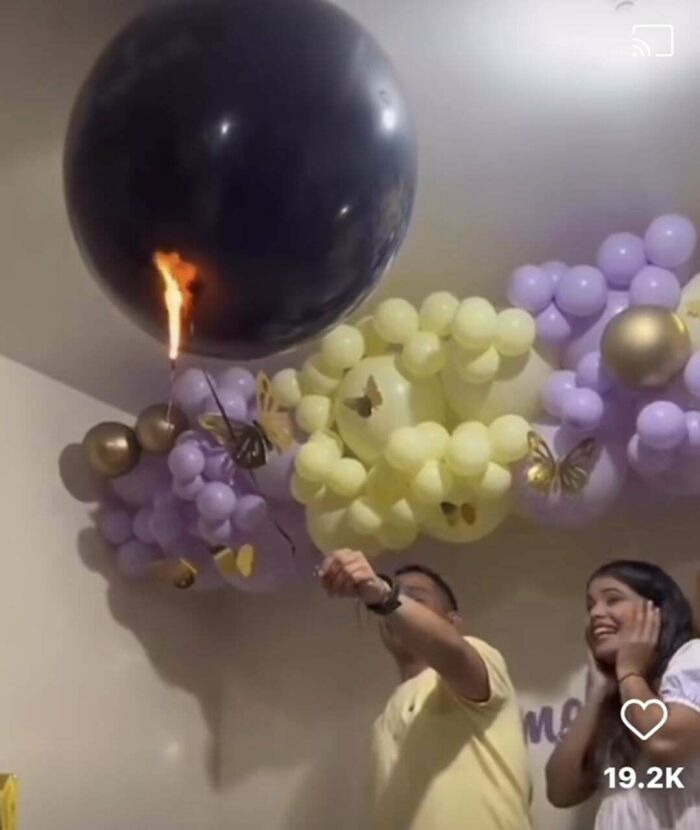 Man holding a lit sparkler near a large black balloon with colorful decorative balloons in the background.