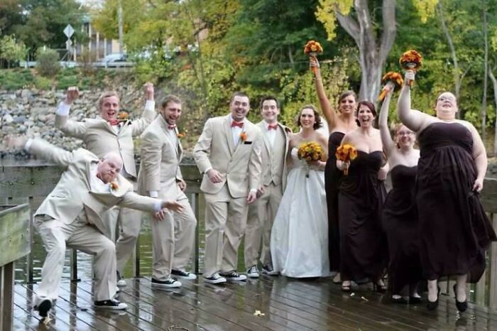 Wedding party caught in a frozen frame with playful poses and joyful expressions by a lakeside dock in autumn.